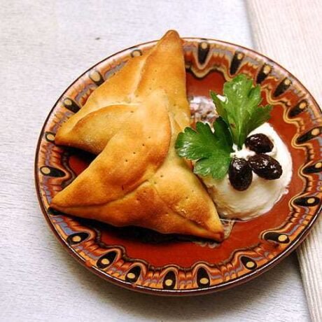 fatayer, czyli arabskie trójkąciki z zielonym nadzieniem podane na zdobionym arabskim talerzyku z kleksem jogurty naturalnego, oliwą, czarnymi oliwkami i natką pietruszki