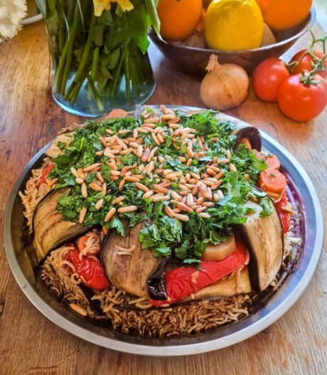 arabska, wegetariańska potrawa makloubeh, czyli jednogarnkowe danie, wyłożone na tacy, obsypane dużą ilością posiekanej natką pietruszki i prażonymi orzeszkami pinii