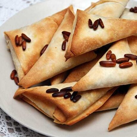 arabskie rożki z ciasta youfka z orzekami pinii, przypieczone na złoty kolor, ułożone w stos na talerzu