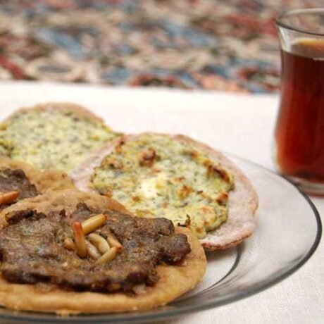 placuszki sfiha z mięsem, posypane orzeszkami pinii i z serem i przyprawami podane na talerzu w towarzystwie gorącej herbaty po arabsku